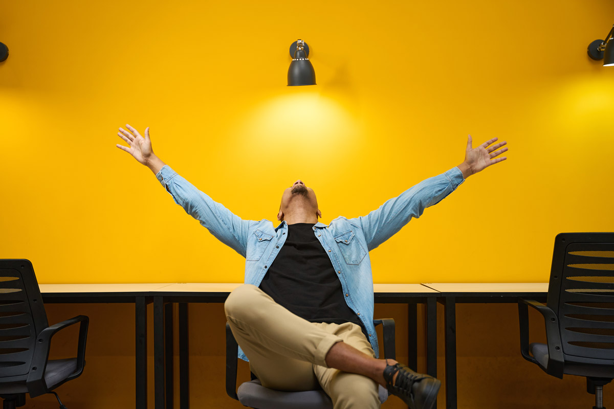 Homme heureux assis sur une chaise et levant les mains en l’air